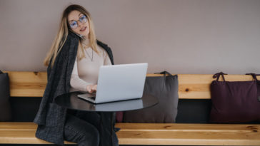 woman sitting at a table talking on a phone and typing on a laptop