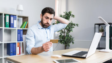 frustrated man in front of a laptop looking at a credit card