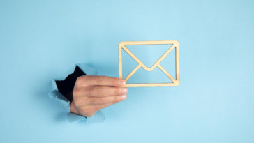 hand coming through a blue wall holding a wooden envelope sign