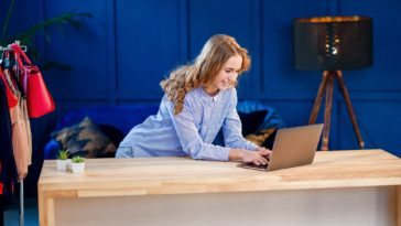 woman using a laptop at a desk with clothes in the background