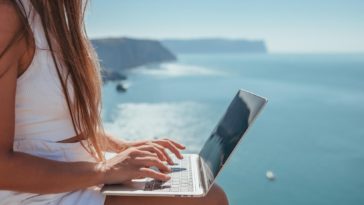 digital nomad woman sits on rocks by the sea