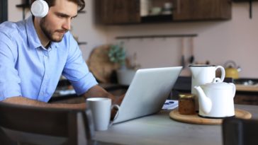 man with headphones working remotely on a laptop from a kitchen