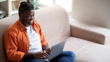 man sitting on a couch working on a laptop from home