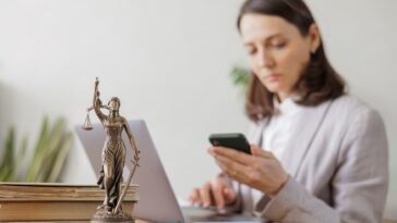 woman sitting in an office looking at her phone with a goddess of justice statuette on the desk