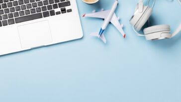 a laptop, model plane, headphones and coffee on a baby blue surface